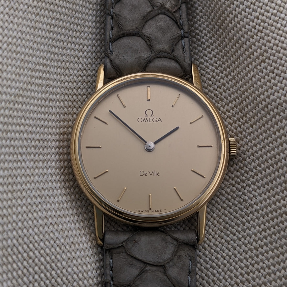Front-facing Omega De Ville reference 111 0156 with cream dial, Omega logo, De Ville text, baton markers, and gray textured strap.