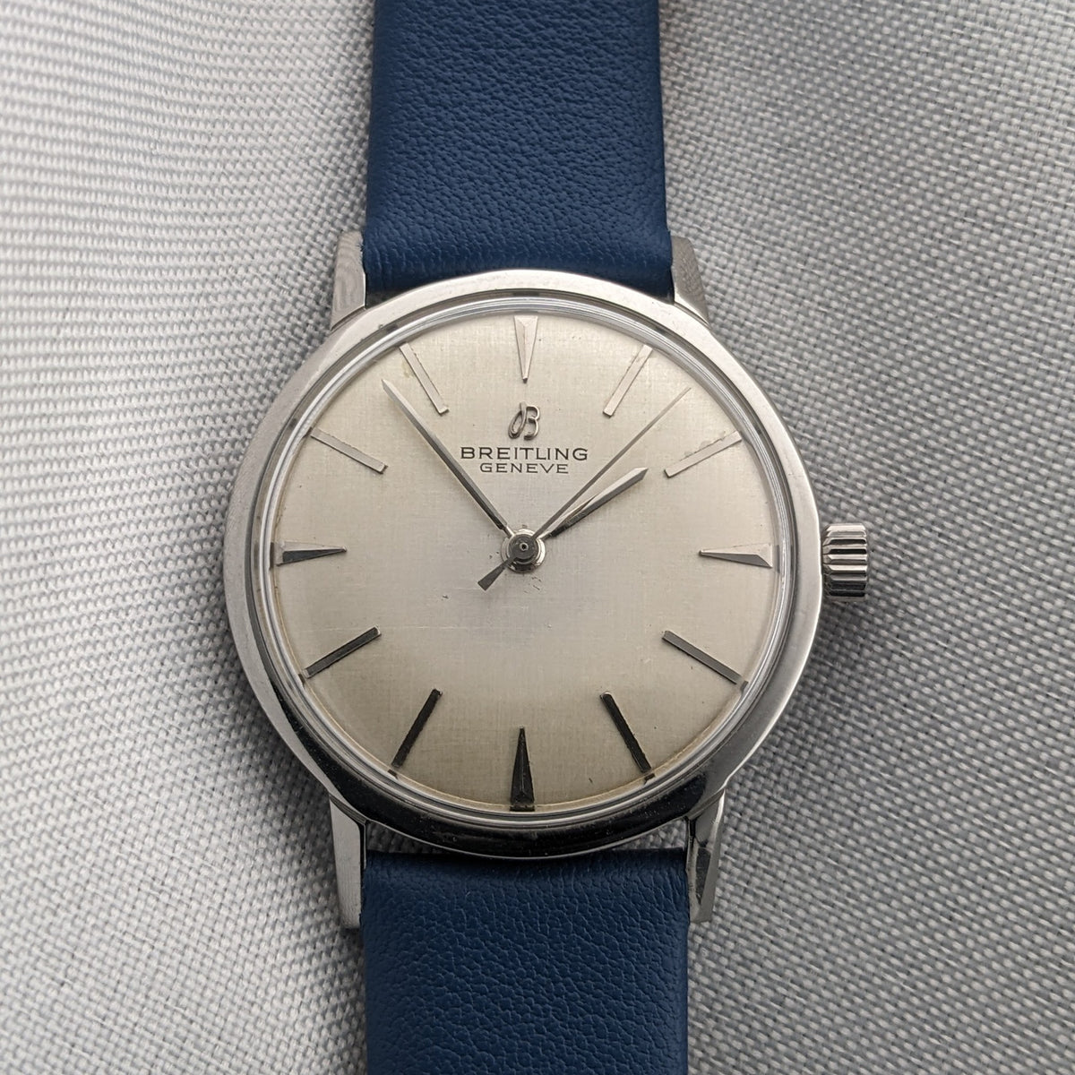Breitling Automatic watch presented vertically with a cream dial, applied hour markers, silver hands and blue leather strap.