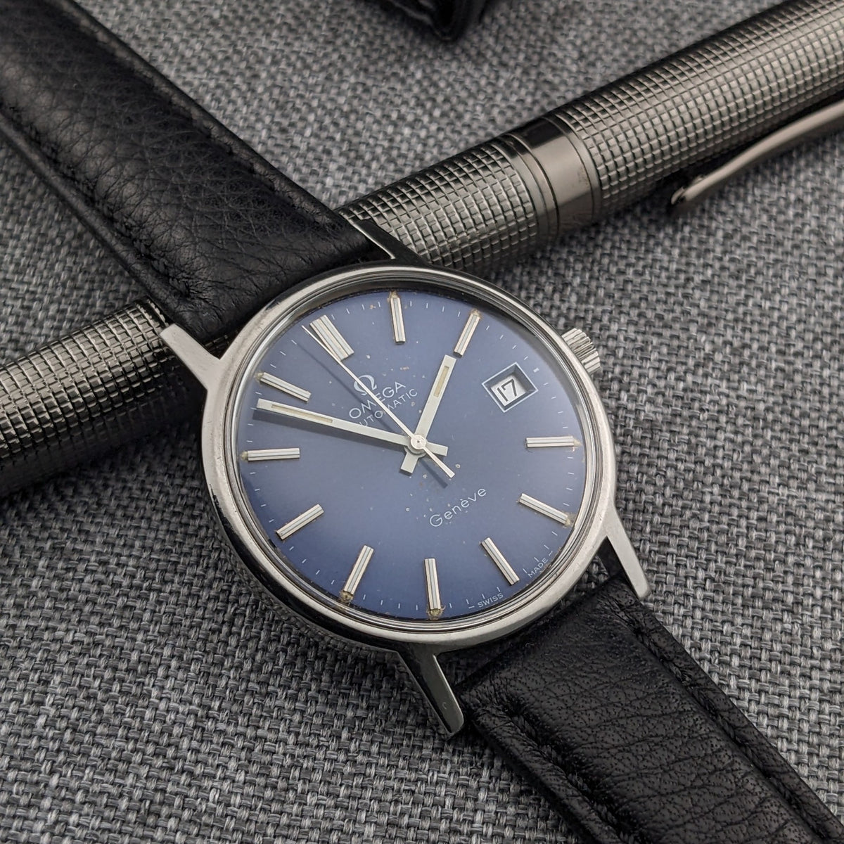 Angled view of the Omega Geneve Automatic reference 166.0163, featuring its blue dial, date display, silver markers and black leather strap.