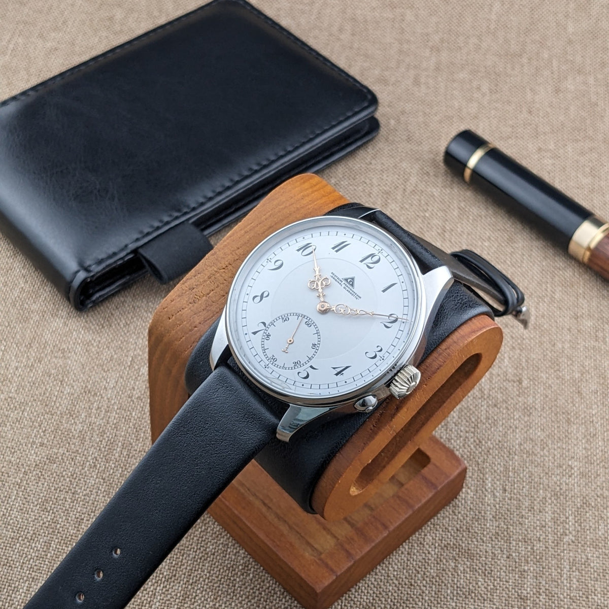 Schrägansicht der Deutsche Präzisionsuhr „Original Glashütte” auf einem Holzhalter neben einem schwarzen Etui und einem schwarz-an