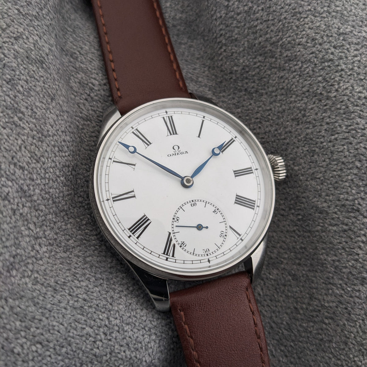 Orologio Omega in orientamento verticale con quadrante bianco a numeri romani, lancette blu, sub-quadrante dei secondi, anse lucide e cinturino marrone cucito.