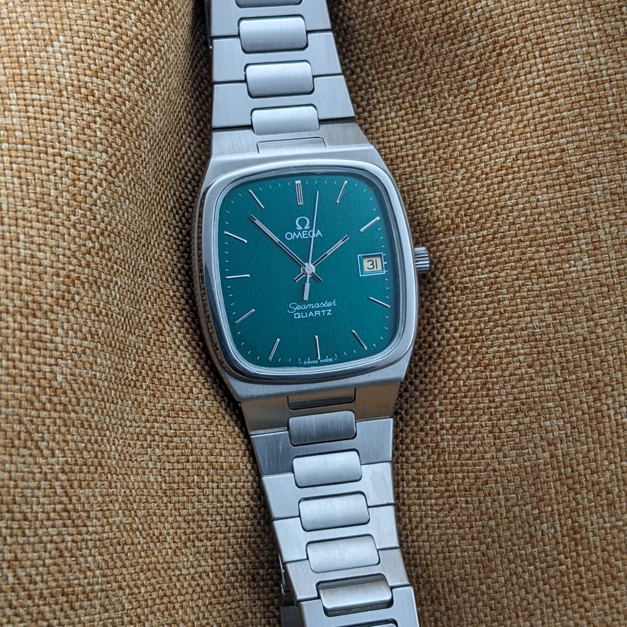 Straight-on view of the Omega Seamaster reference 196.0166 teal dial, date display, hands, rounded rectangular case, and stainless-steel bracelet.