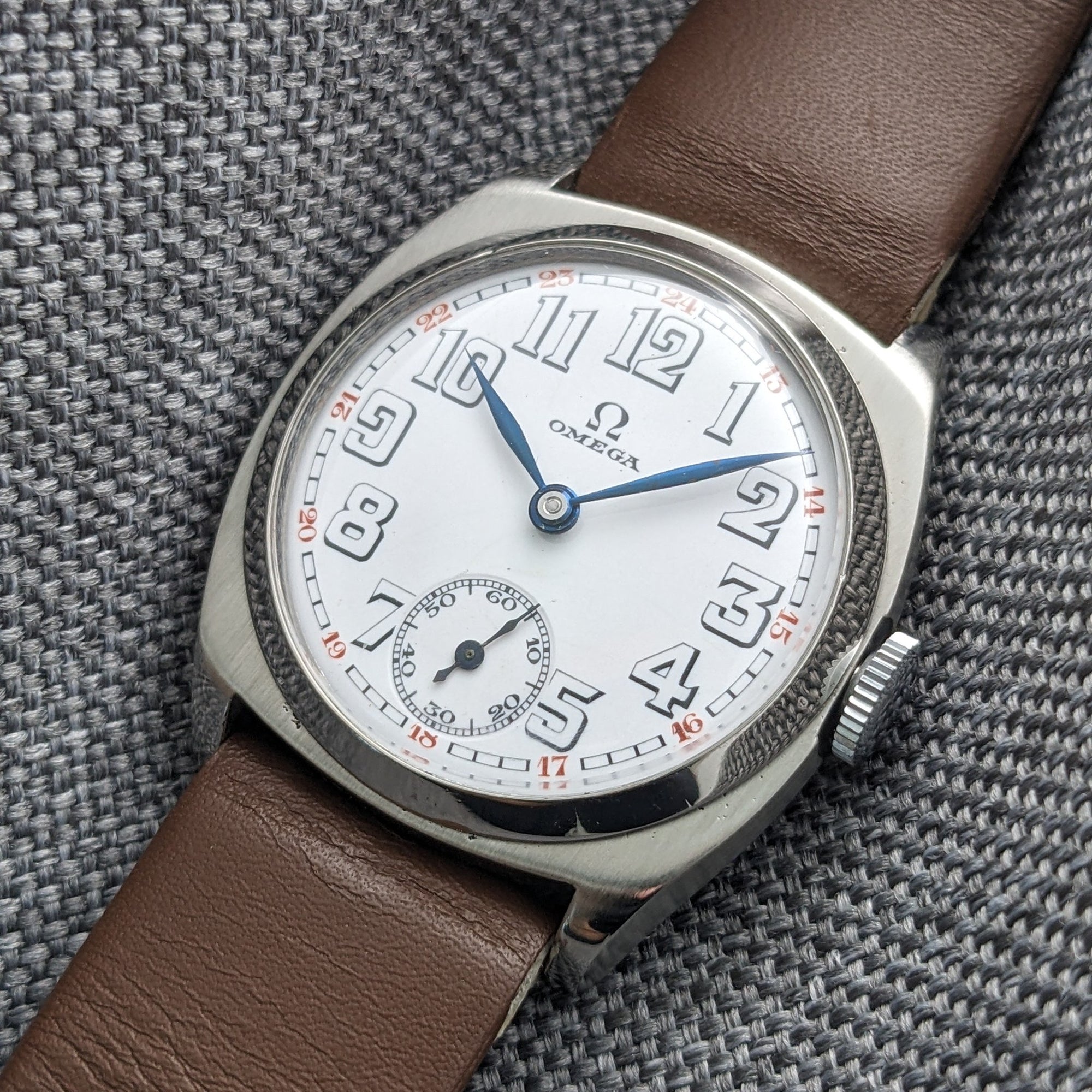 Close-up of an Omega watch dial featuring large Arabic numerals, red minute markings, blue hands, and a small seconds subdial.