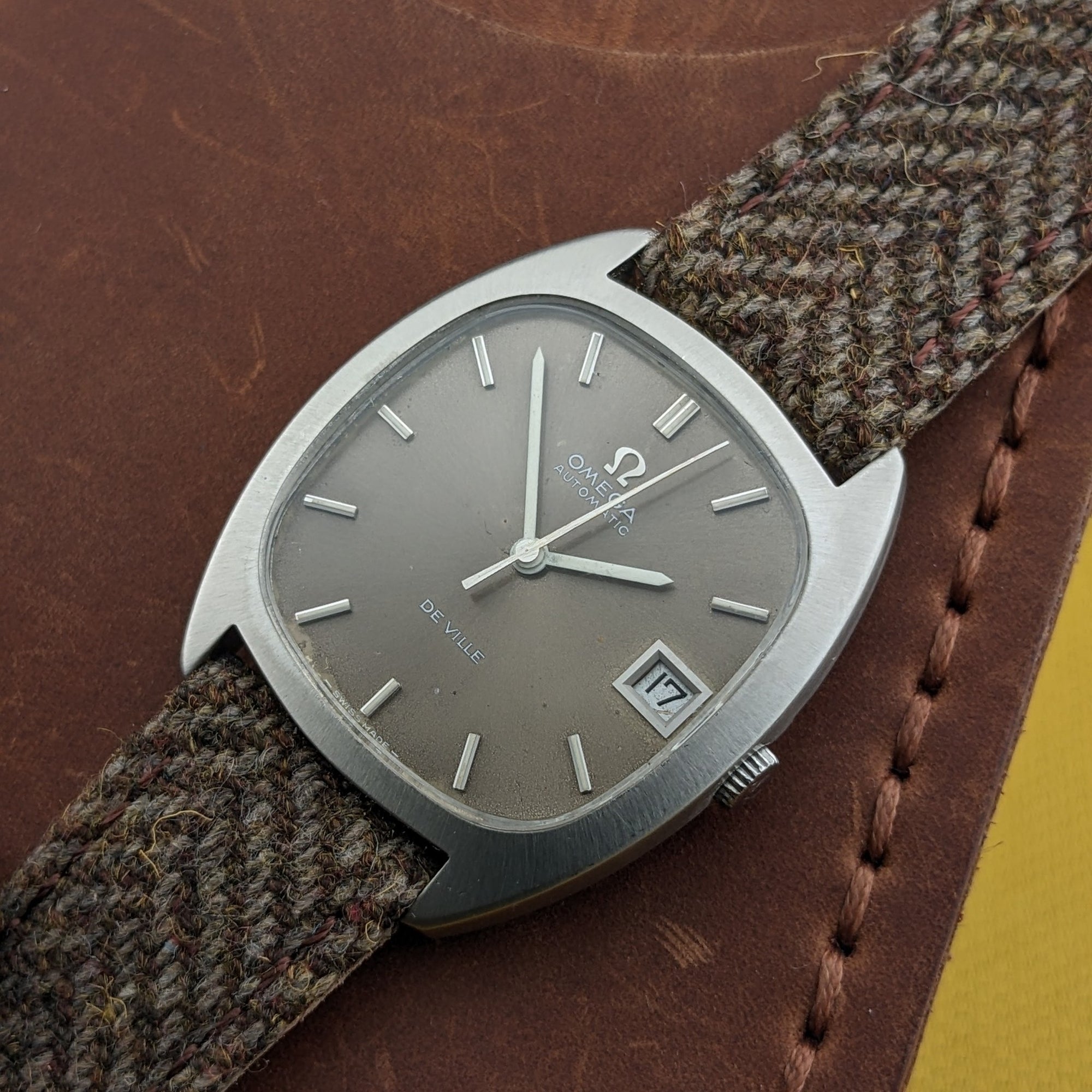 Angled close-up of the Omega Dr Ville Automatic ref. 162.045, showing its silver dial, applied markers, date display, crown, and woven strap.