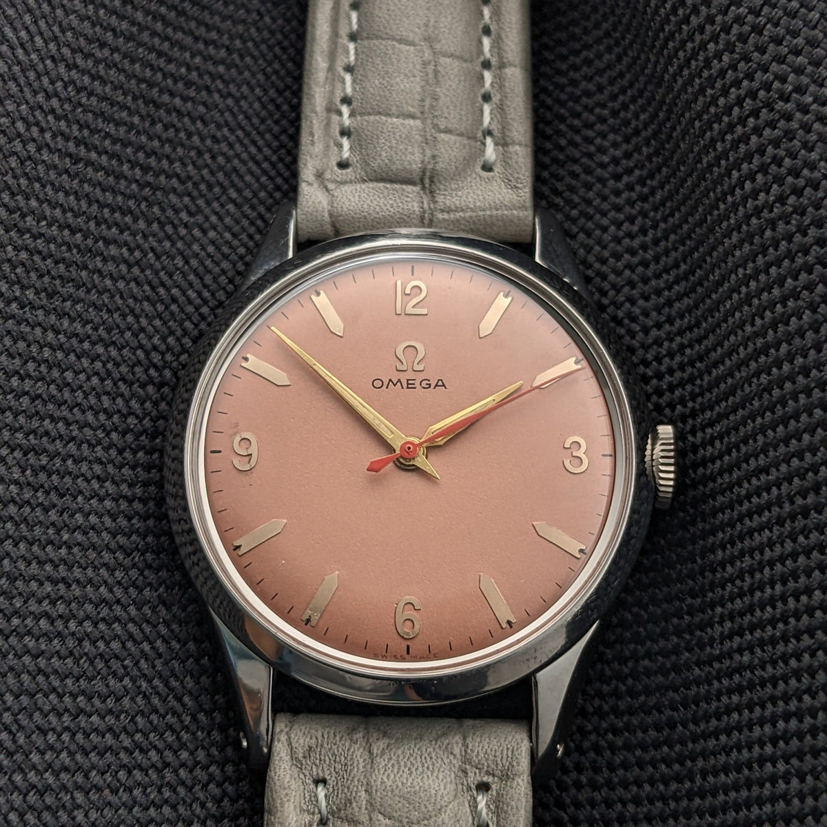 Frontalansicht der Omega Classic 2760-6 SC Nahaufnahme mit rosafarbenem Zifferblatt, 12-3-6-9 Zahlen, Balkenindizes und grauem Lederarmband.