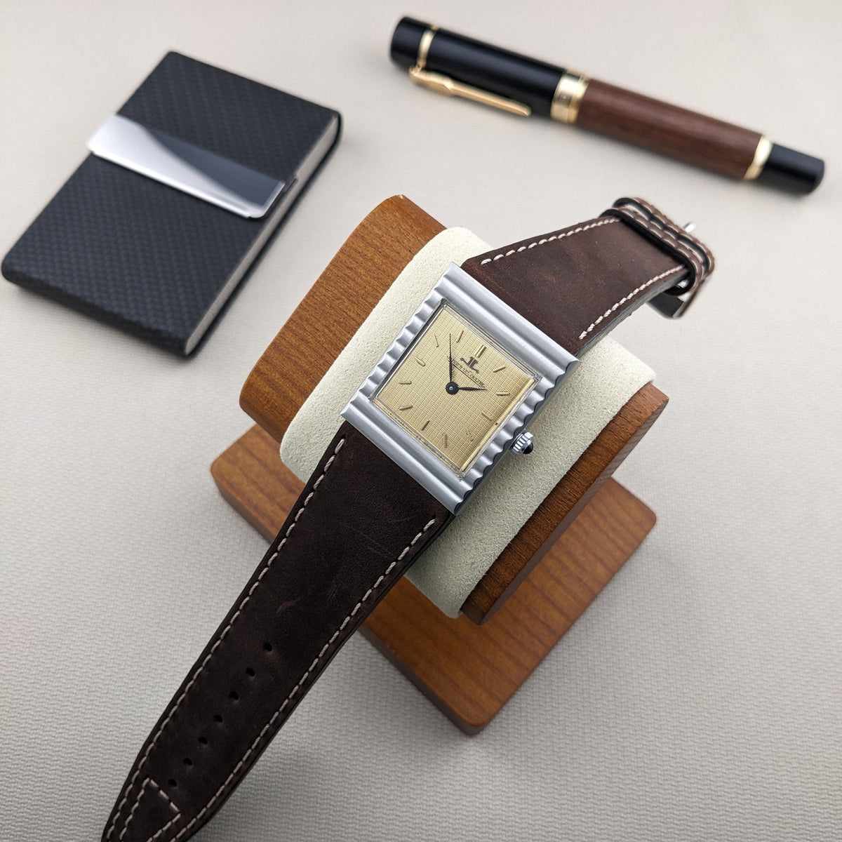 Jaeger-LeCoultre Vogue Tank Ref. 9120 auf einem Holz-Uhrenständer neben einem schwarzen Notizbuch und einem Holz-Schwarz-Stift.