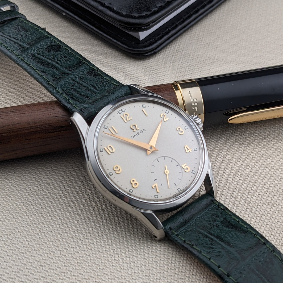 Vista angolata dell'OMEGA Classic referenza 2639-11, con quadrante argentato, numeri dorati, cinturino verde e penna in legno e nero.