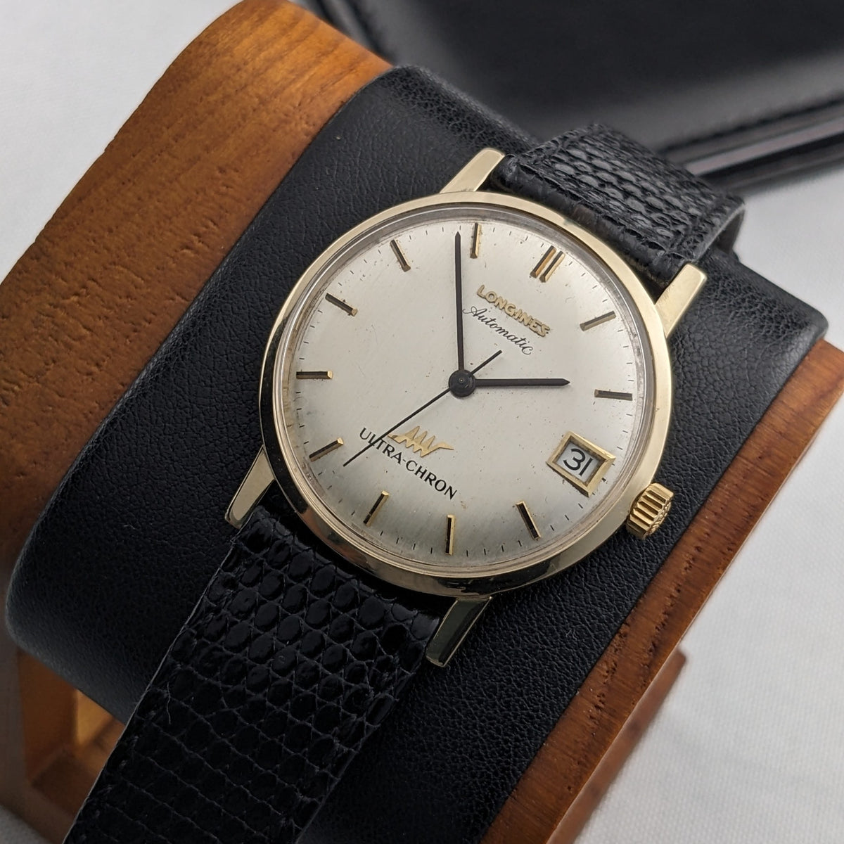 Longines Ultra-Chron 69-556AC displayed diagonally on a black and brown leather cushion, with cream dial and date window visible.