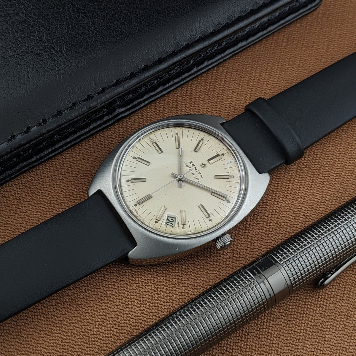Close view of the Zenith Automatic reference GR 720001 dial with baton markers, date window, black strap, and silver pen.