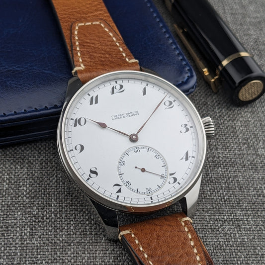 Ulysse Nardin Locle & Genève घड़ी नीले चमड़े के केस और काले लेखन उपकरणों के साथ प्रदर्शित, डायल ऊपर की ओर।