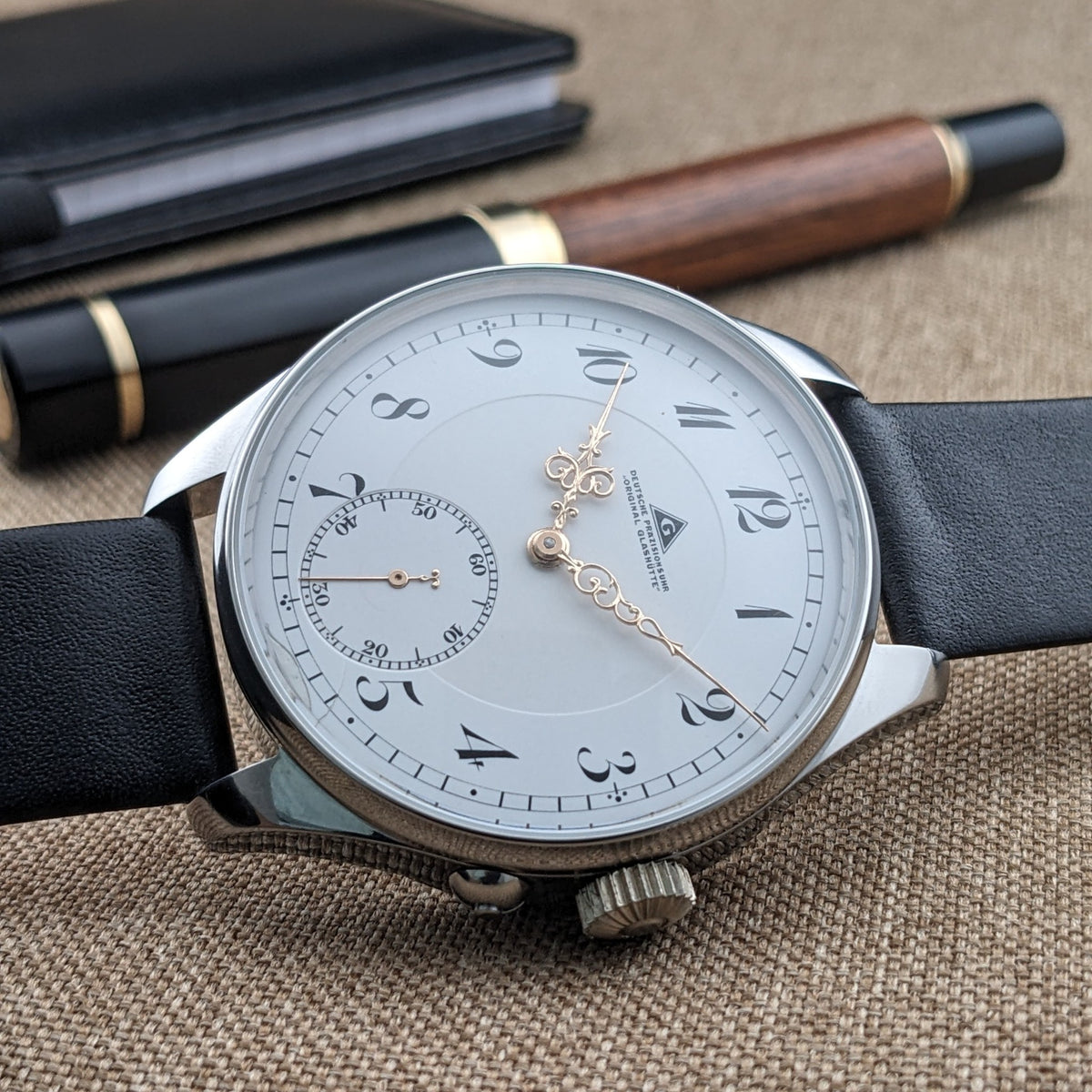 Deutsche Präzisionsuhr „Original Glashütte” liegt horizontal auf Stoff, mit weißem Zifferblatt, kleiner Sekunde und s