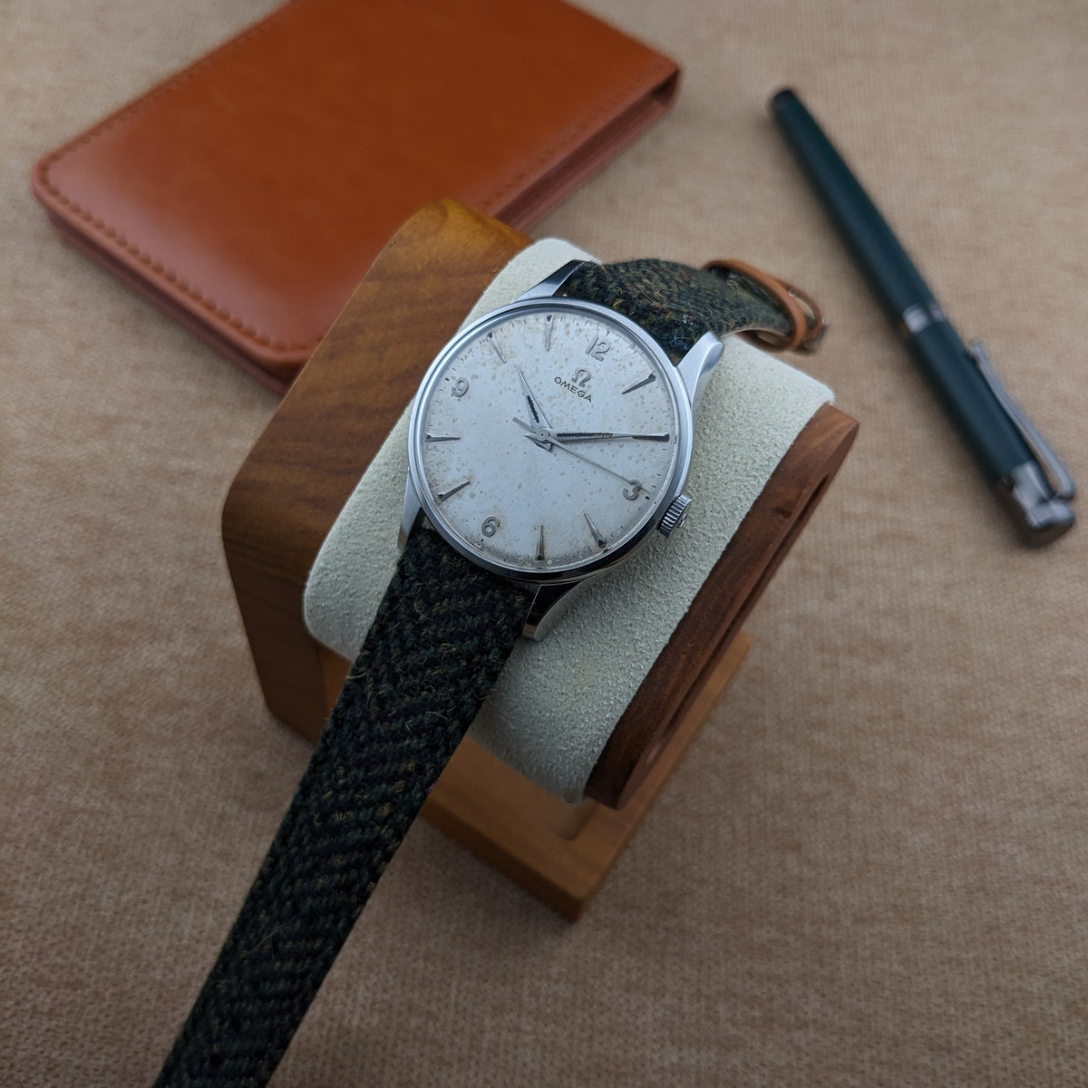 Omega Classic Referenz 2810-2 SC auf einem Holzuhrenständer, mit einem braunen Notizbuch und dunklem Stift im Hintergrund.