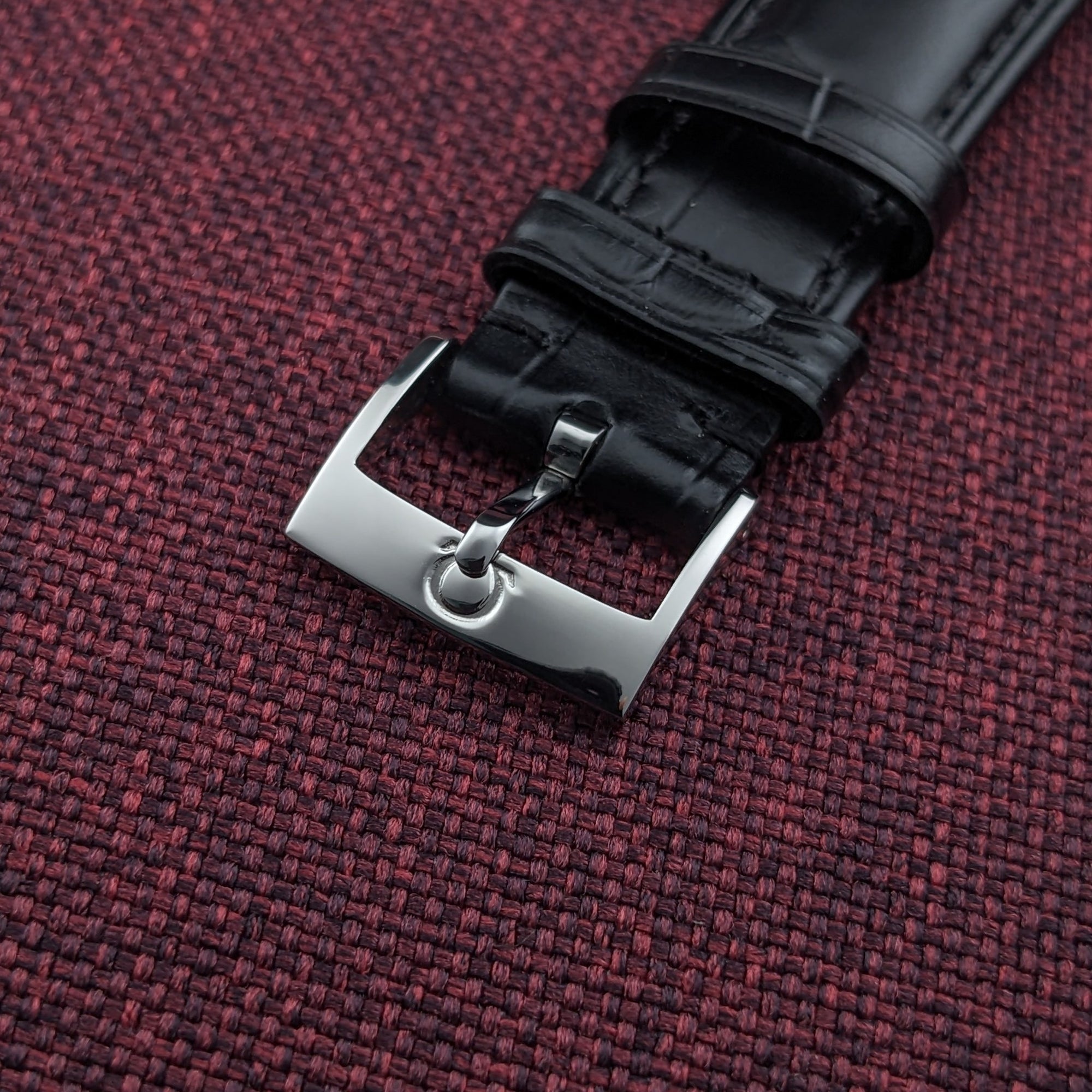 Omega Genève reference 131.022 black leather strap ending in a polished rectangular buckle, shown against burgundy fabric.