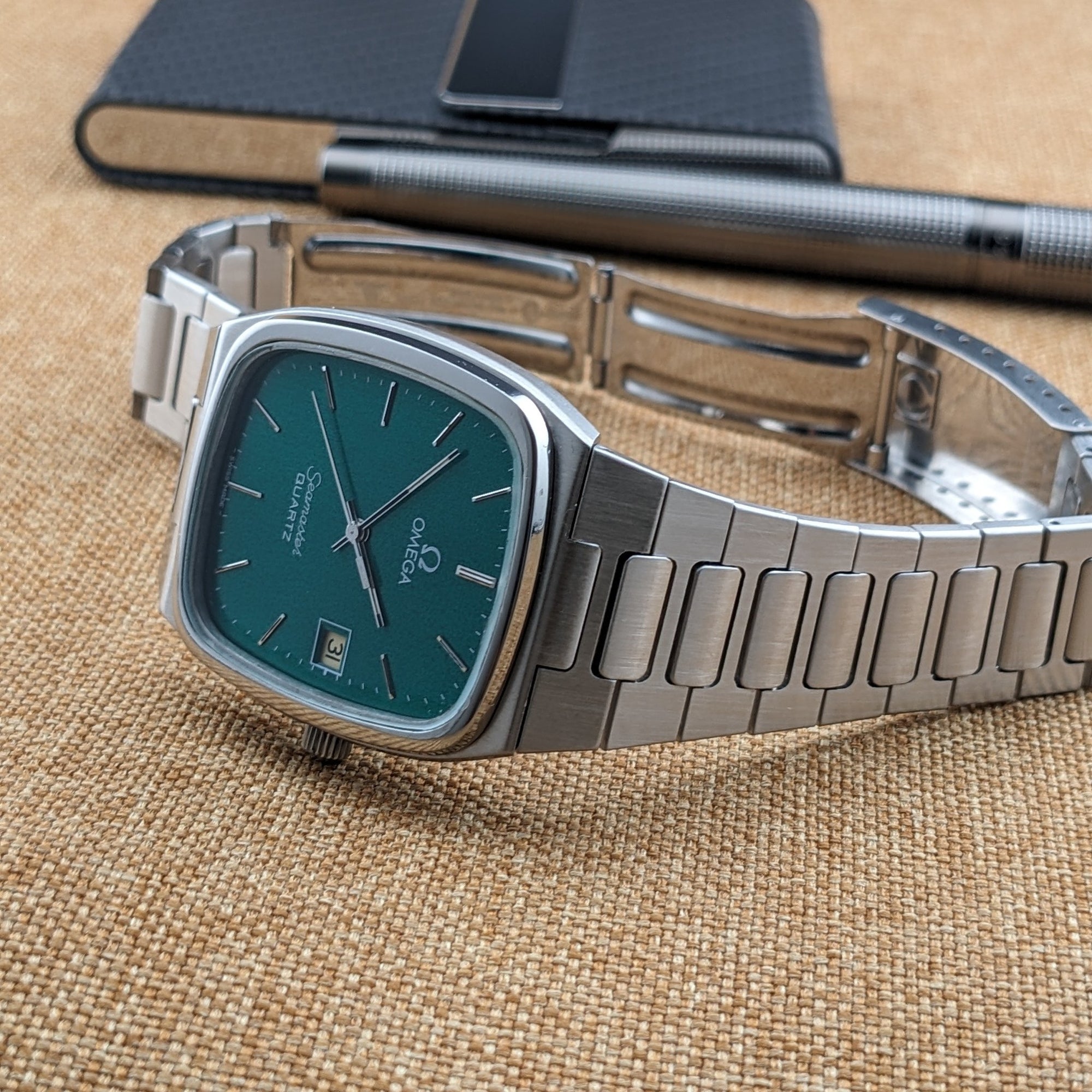 Omega Seamaster reference 196.0166 shown at an angle with teal dial and bracelet, alongside a black pen and loose metal bracelet parts.