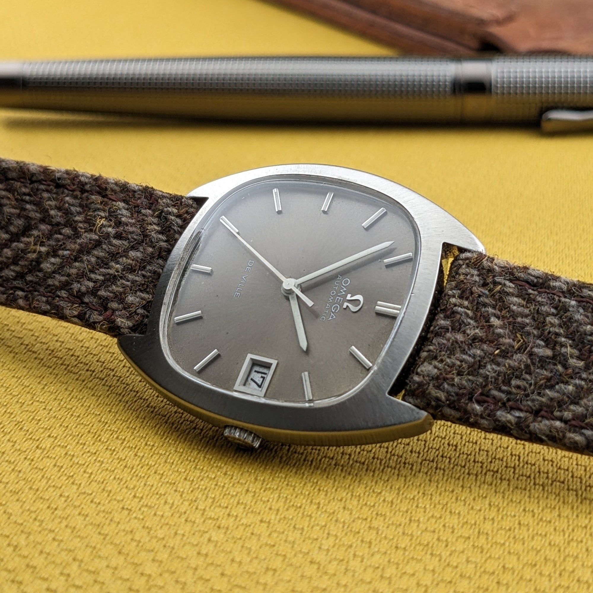 Omega Dr Ville Automatic ref. 162.045 viewed at a low angle on yellow fabric, with the silver dial and brown woven strap prominent.
