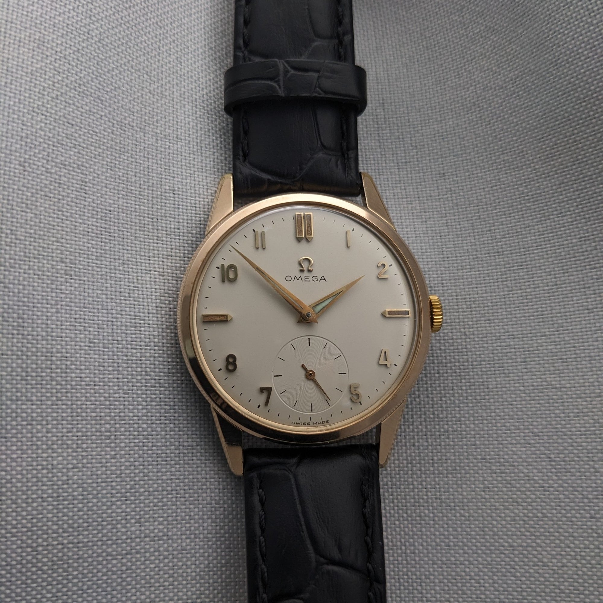 Omega Classic reference 14391-1 presented vertically on gray fabric, displaying the light dial, gold-tone case and black leather strap.