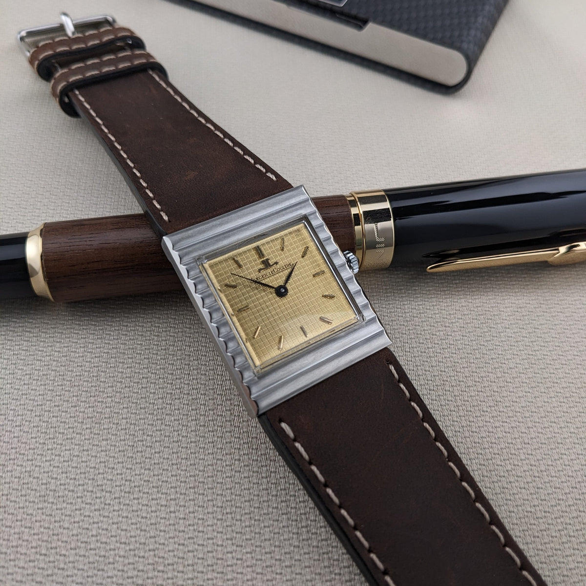 Jaeger-LeCoultre Vogue Tank Ref. 9120 über einem Holz-Schwarz-Stift, mit ihrem braunen genähten Armband und dem silberfarbenen Gehäuse gut sichtbar.