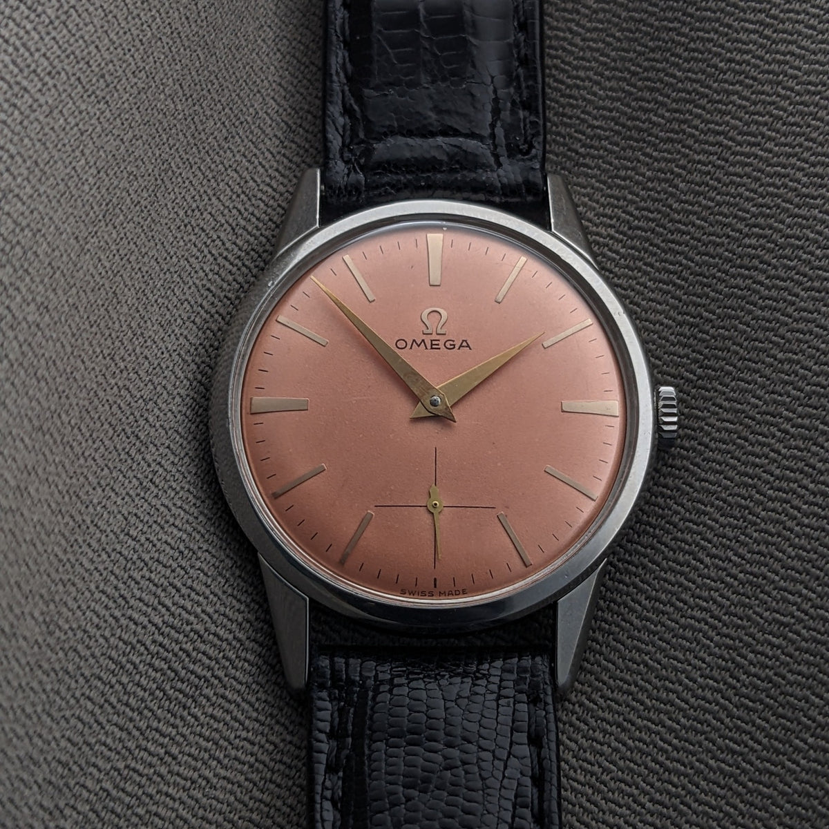 Omega Classic referenza 14391-1 fotografato verticalmente su tessuto grigio, con quadrante rosa, cassa argento, cinturino nero e lancette centrali.