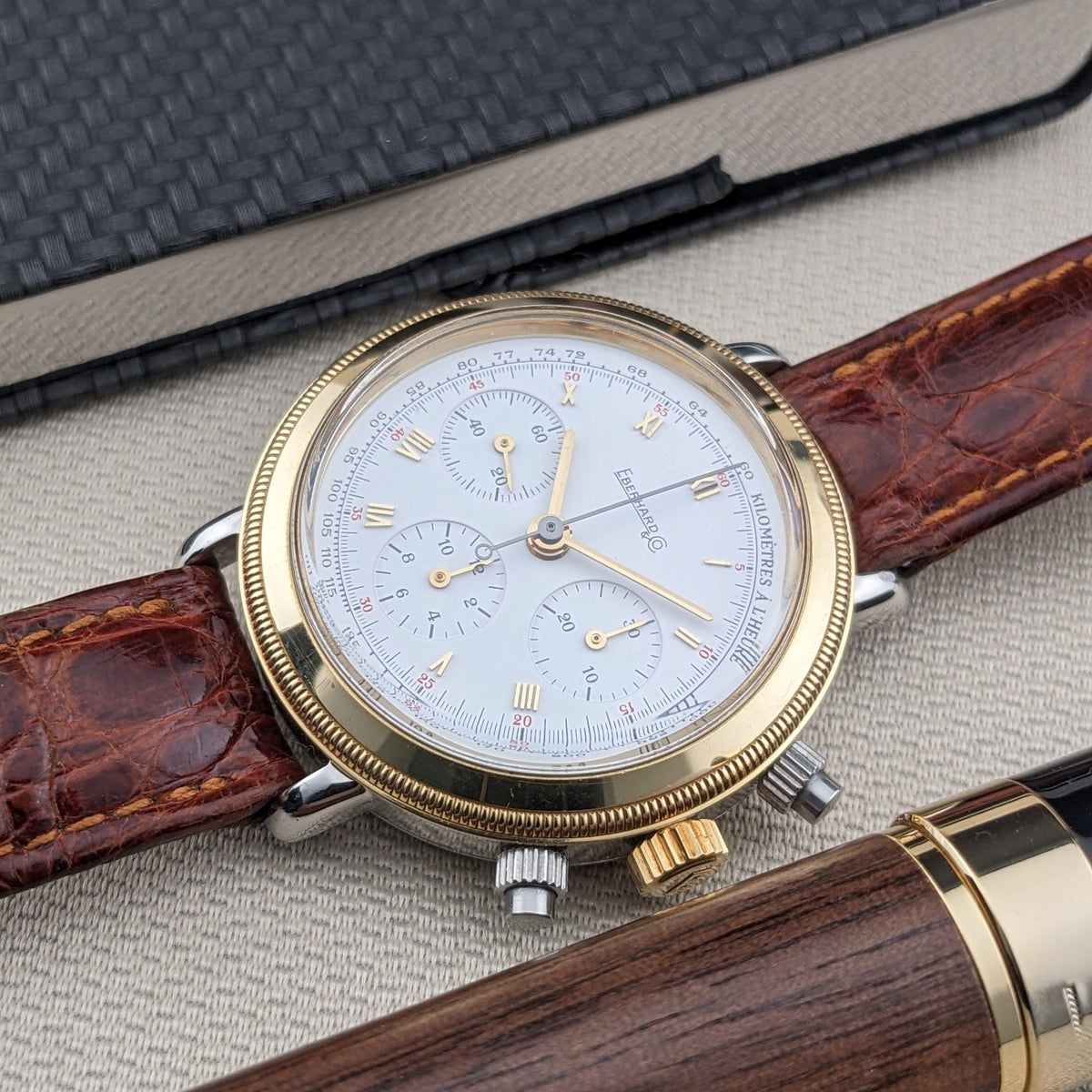Eberhard & Co.. Godron Chrono reference 32031 is pictured diagonally beside an open notebook and wooden fountain pen, with the dial clearly visible.