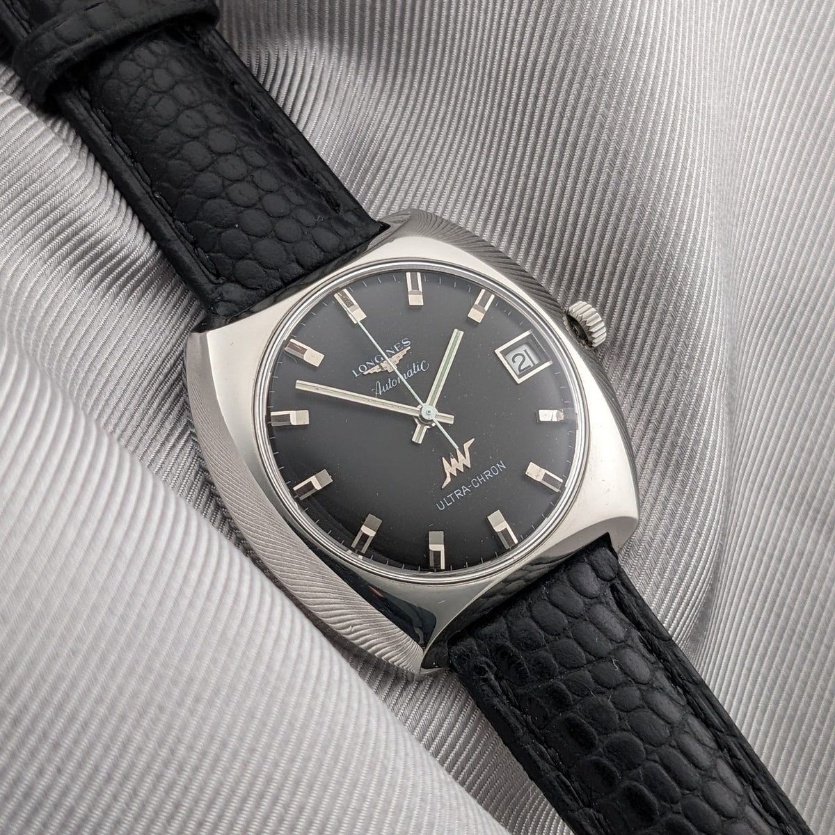 Angled dial view of the Longines Ultrachron reference 8429 with dark face, date display, baton markers and black textured leather strap.