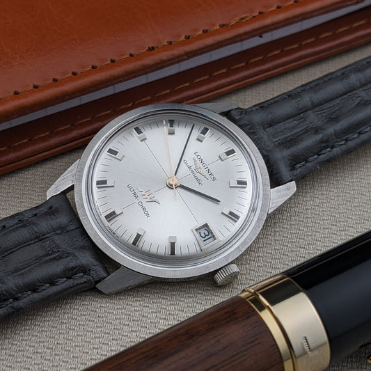 Close view of the Longines Ultra-Chron 7827 silver dial, applied hour markers, date display, and black leather strap beside a leather case.