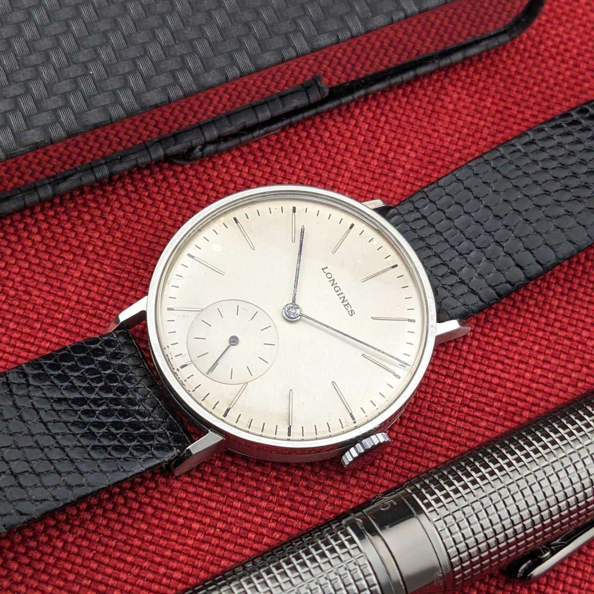 Angled view of the Longines Calatrava reference 20757 dial and black textured strap, with a silver pen and notebook in the background.