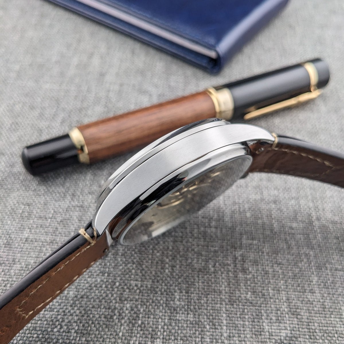 Ulysse Nardin कलाई घड़ी का साइड प्रोफाइल, जिसमें चमकदार केस एज, क्रिस्टल, लग्स और भूरा चमड़े का पट्टा दिखता है।