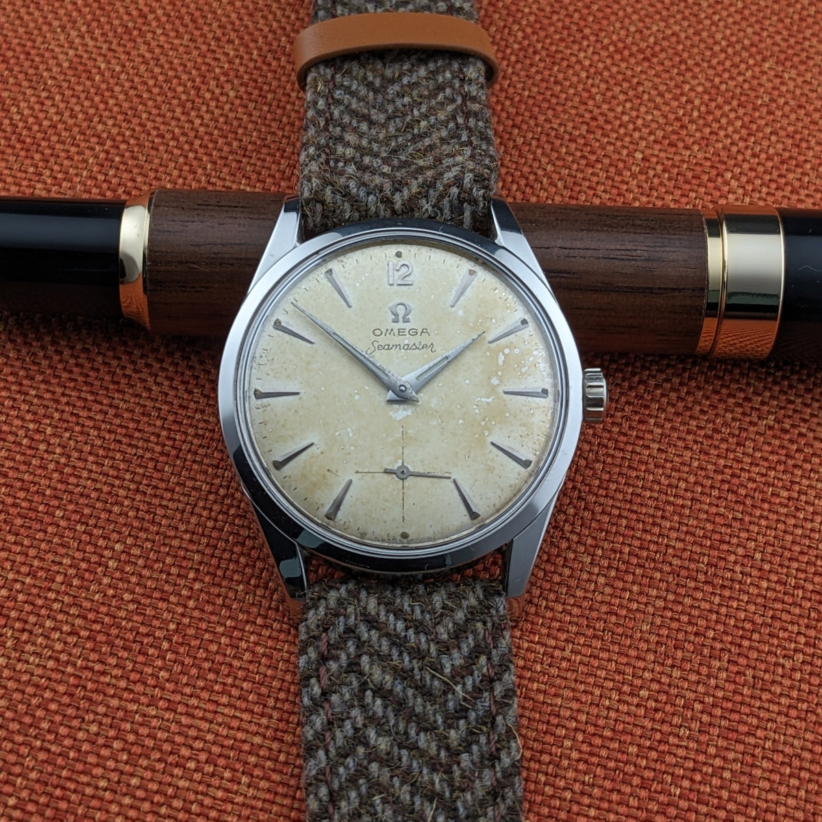 Omega Seamaster reference 29374 laid across a wood-and-black pen, showing the cream dial, hour markers, hands, seconds subdial and woven strap.
