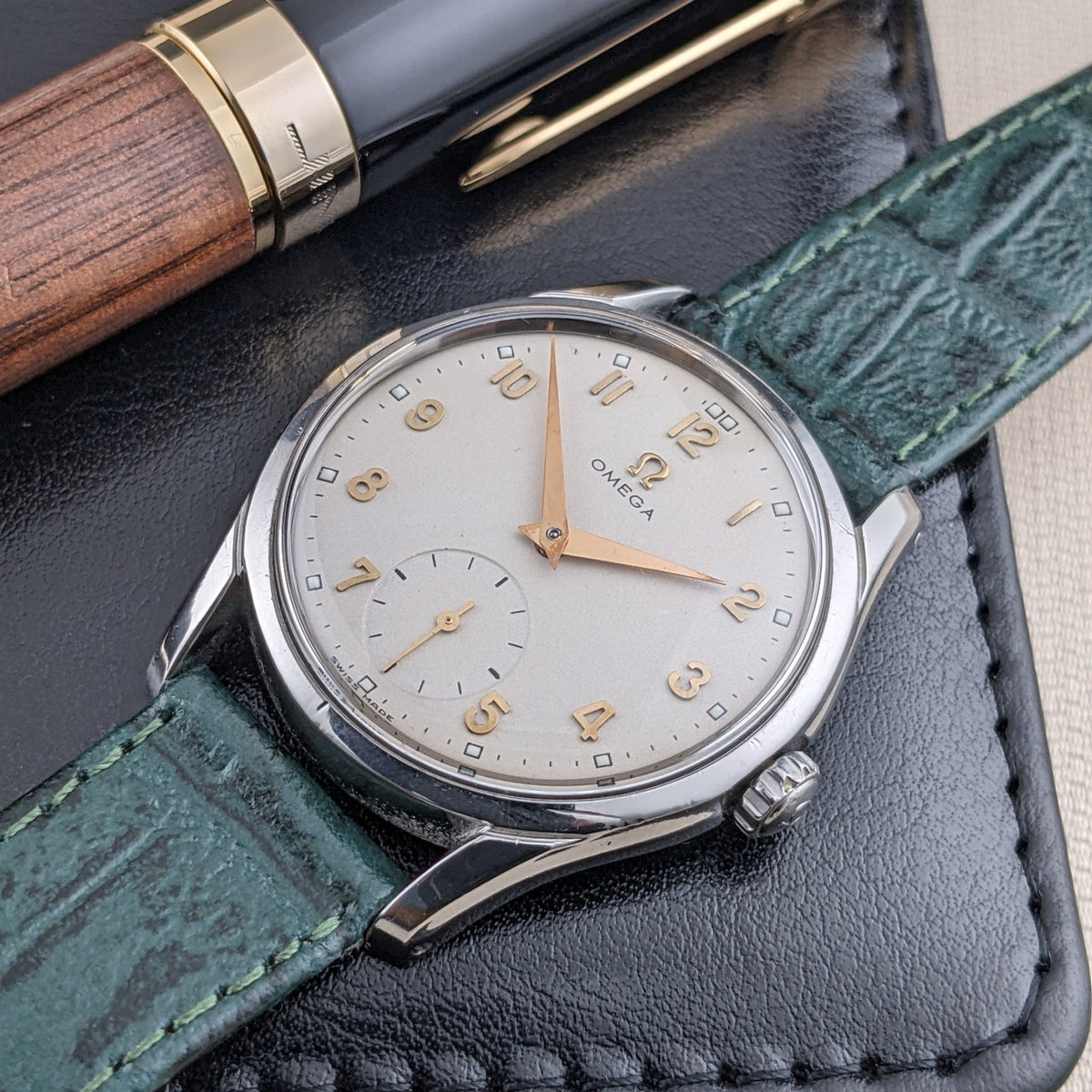 Dettaglio del quadrante OMEGA Classic referenza 2639-11 su una custodia in pelle nera accanto a una penna in legno e nero, con cinturino verde.