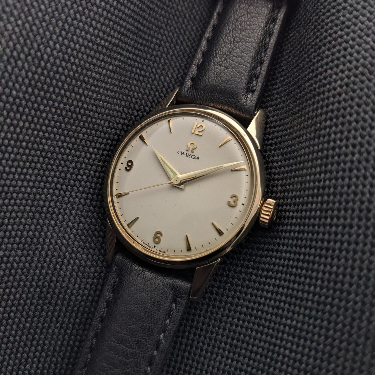 Omega Classic référence 14392-61-SC photographiée en angle, mettant en valeur le cadran crème, les index dorés, la couronne et le bracelet en cuir noir.