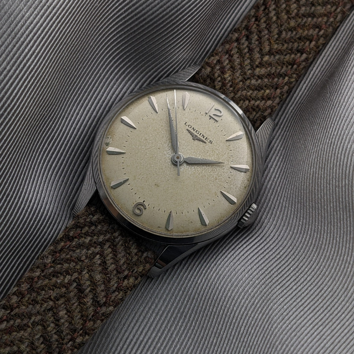 Angled dial view of the Longines Classic reference 8135-5 on gray fabric, showing the cream face, hands, hour markers and brown woven strap.