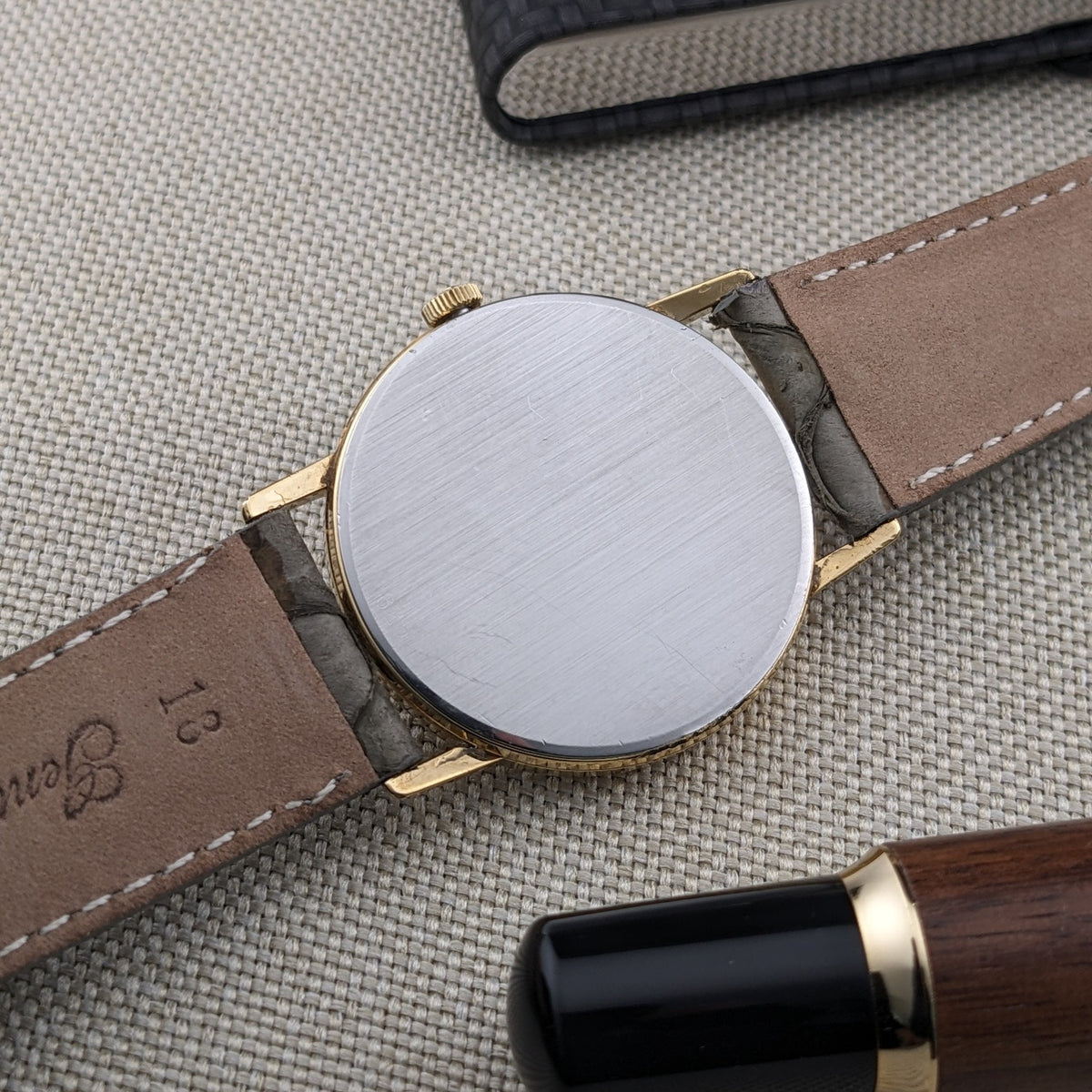 Rear view of Omega De Ville reference 111 0156 with a plain circular metal caseback, gray strap, and gold-tone lugs.