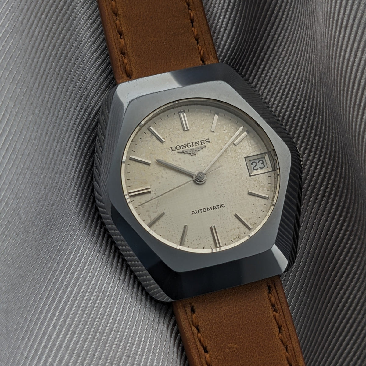 Close-up of the LONGINES Automatic reference 3042-633 on a dark pleated surface, showing the cream dial and date window marked 23.