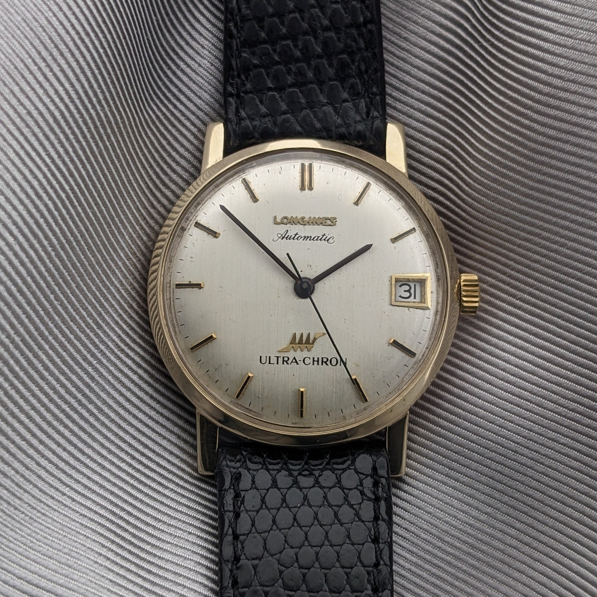 Straight-on view of the Longines Ultra-Chron 69-556AC with cream dial, gold-tone hour markers, date window, and black textured strap.