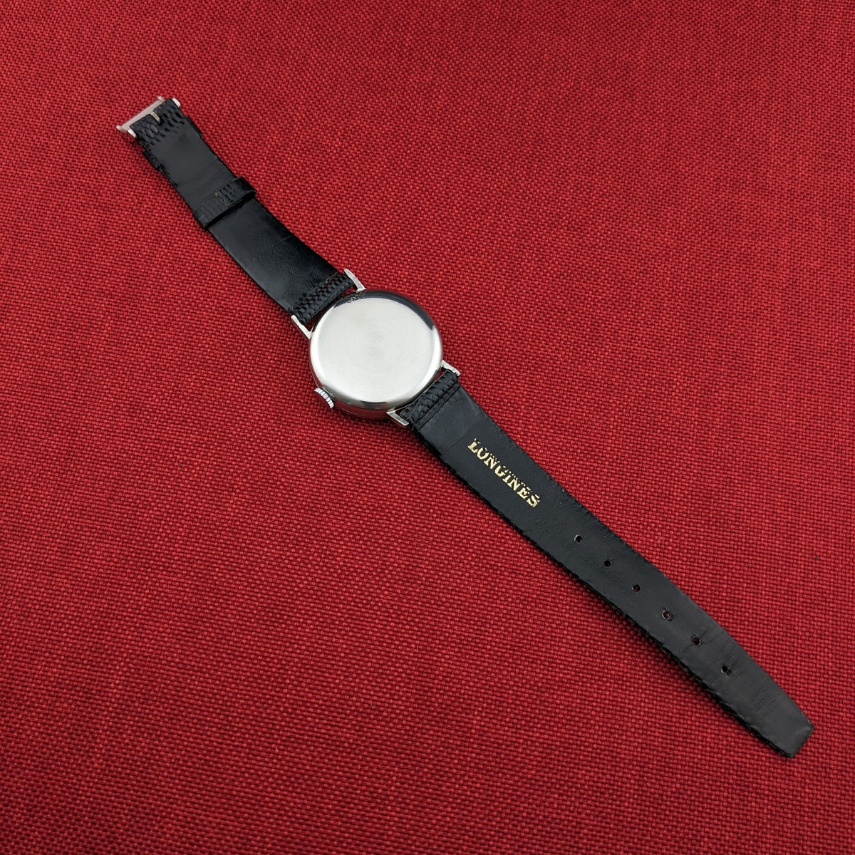 Longines Calatrava reference 20757 shown from the back on red fabric, with the black strap, buckle, and gold Longines lettering visible.