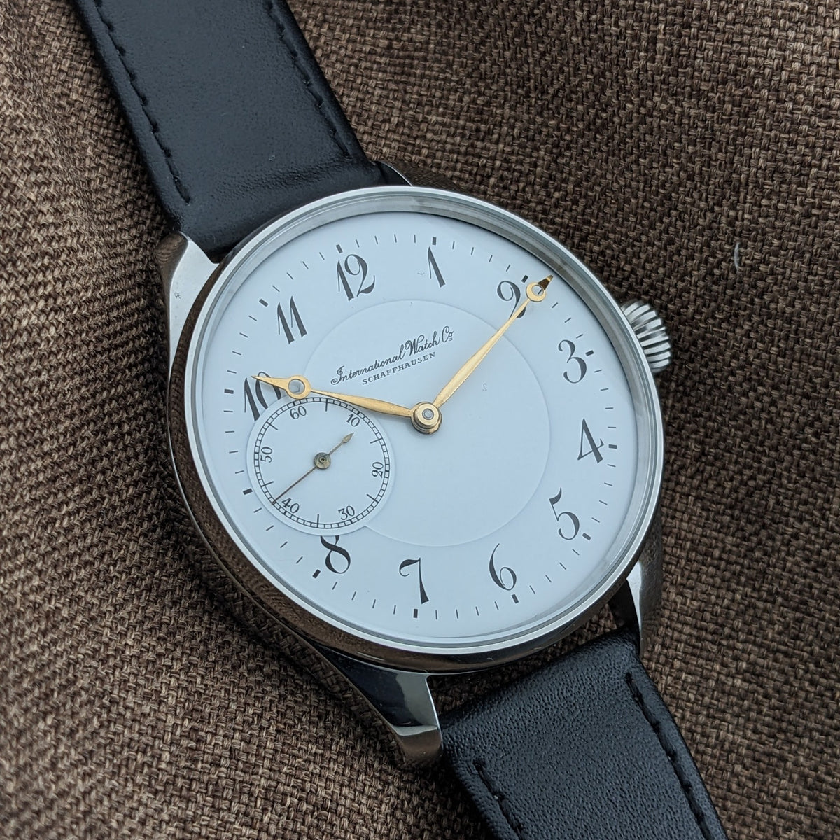 IWC Schaffhausen सफेद डायल का क्लोज़ दृश्य, मुद्रित Schaffhausen स्क्रिप्ट, सुनहरे हाथ, स्टाइलाइज्ड अंक और सेकंड्स सबडायल के साथ।