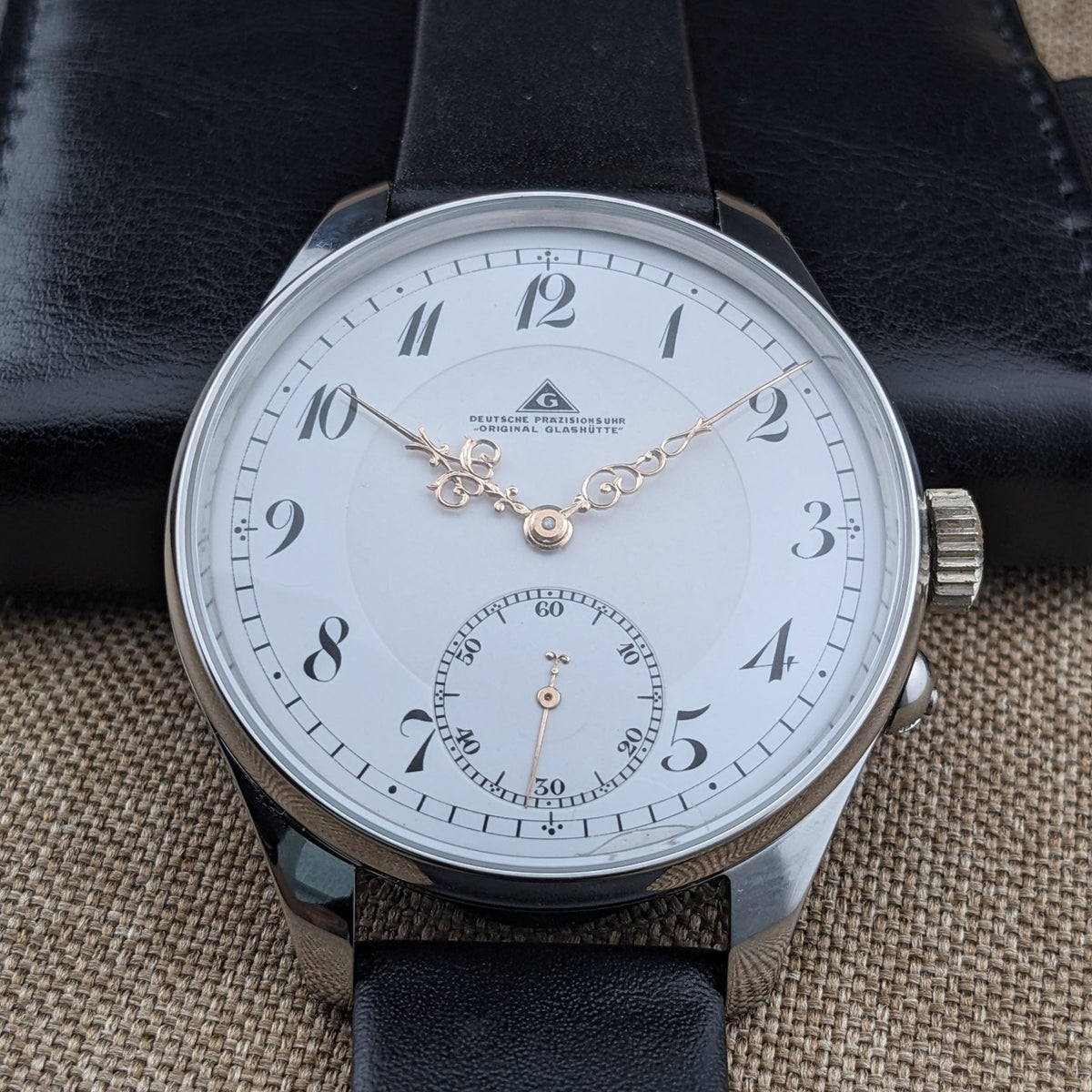 Nahe Vorderansicht der Deutsche Präzisionsuhr „Original Glashütte”, zeigt den gedruckten Zifferblatttext, verzierte Zeiger, Ziff