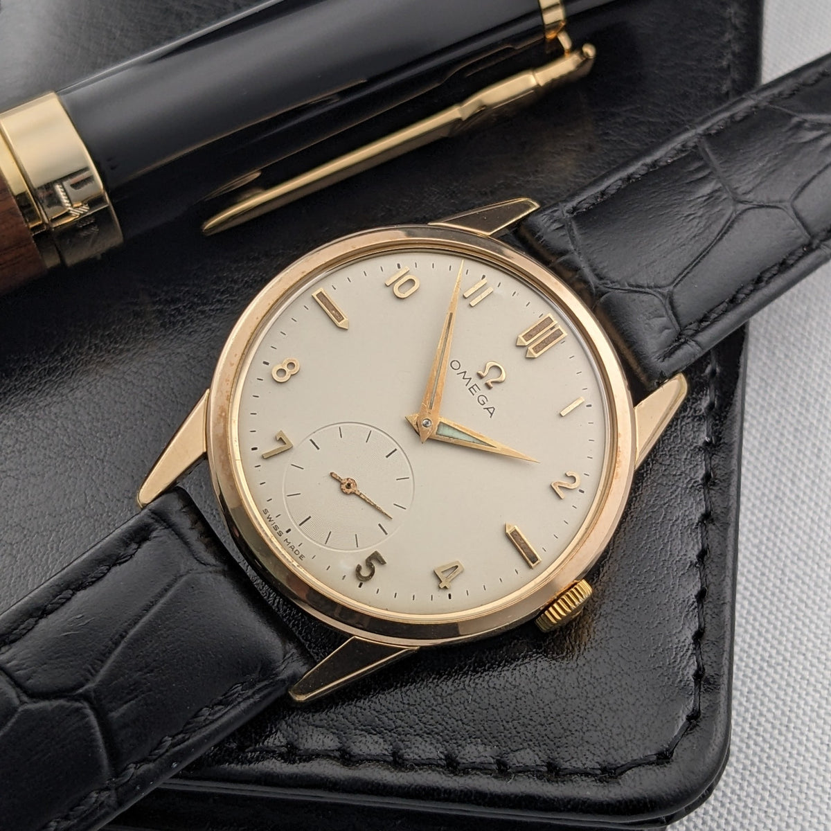 Angled close-up of the Omega Classic reference 14391-1 on a black leather case, highlighting the light dial and small-seconds subdial.