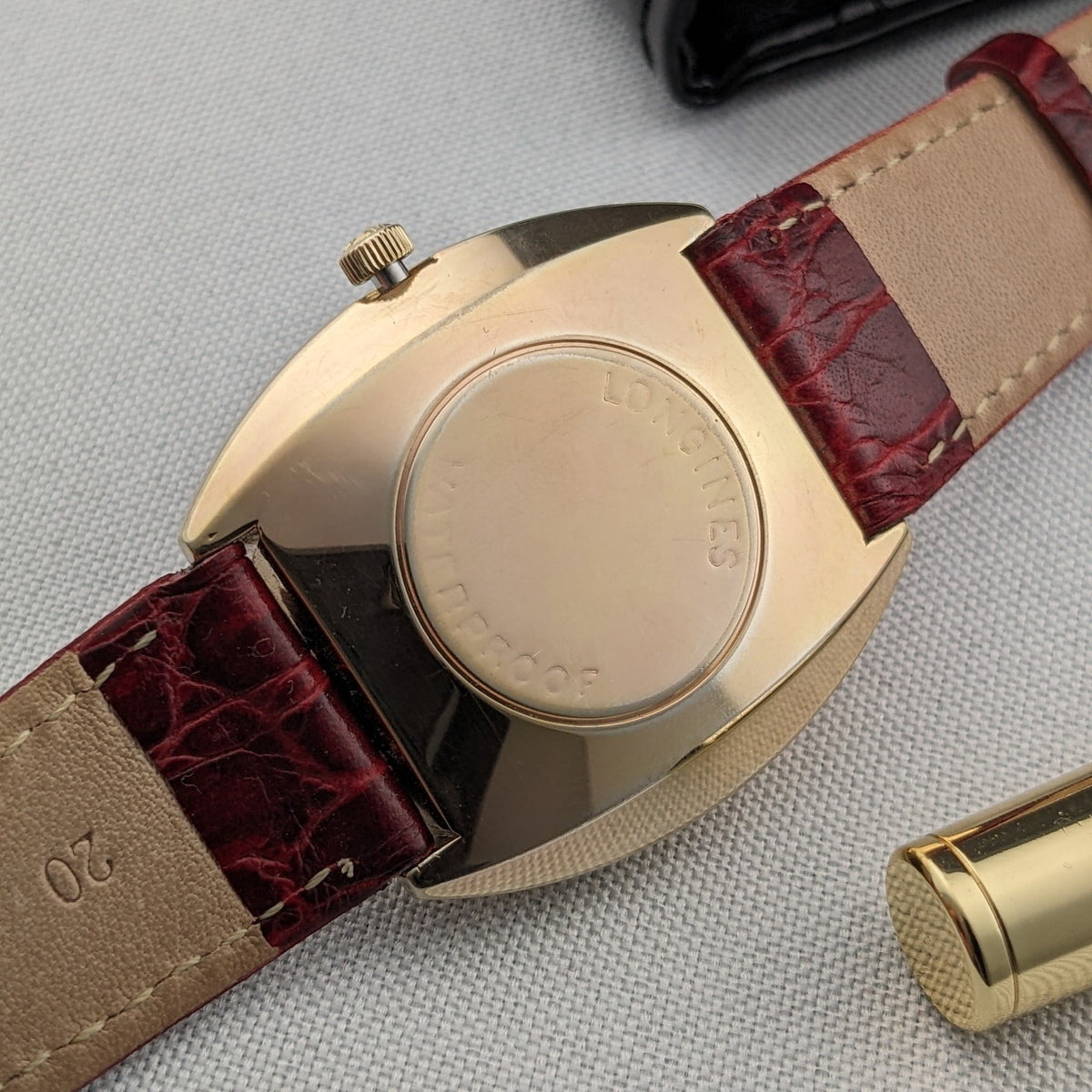 Rückansicht der Longines Admiral 8343-1 zeigt den runden goldfarbenen Gehäuseboden, das burgunderrote Armband und die geprägte zentrale Beschriftung.