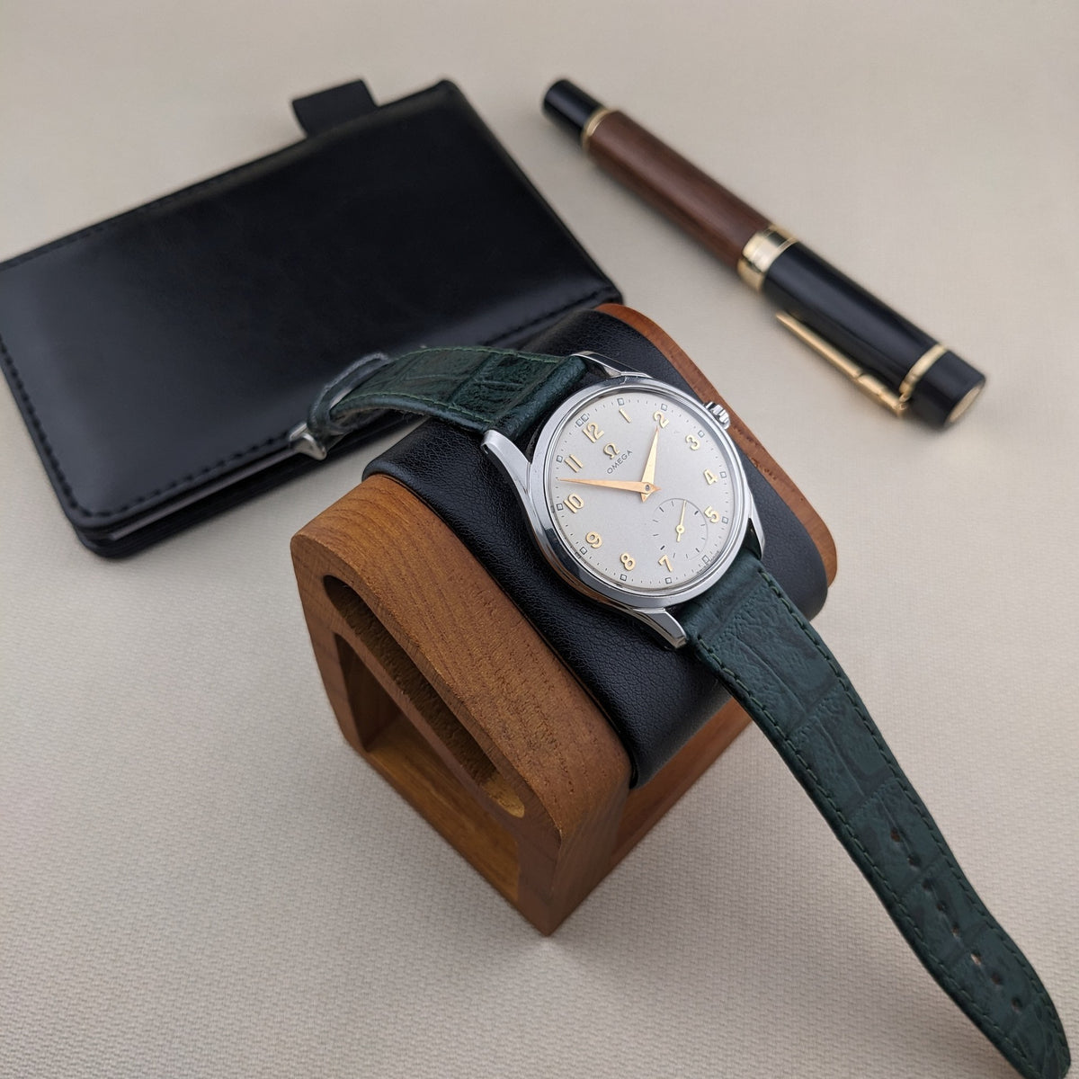 OMEGA Classic 2639-11 su un supporto per orologi in legno con cinturino verde, custodia in pelle nera dietro e penna in legno e nero sullo sfondo.