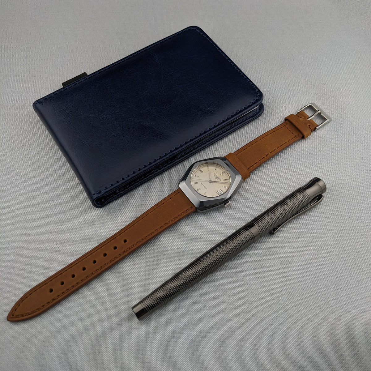 LONGINES Automatic reference 3042-633 laid out with its brown strap, blue case and textured metal pen on a light surface.