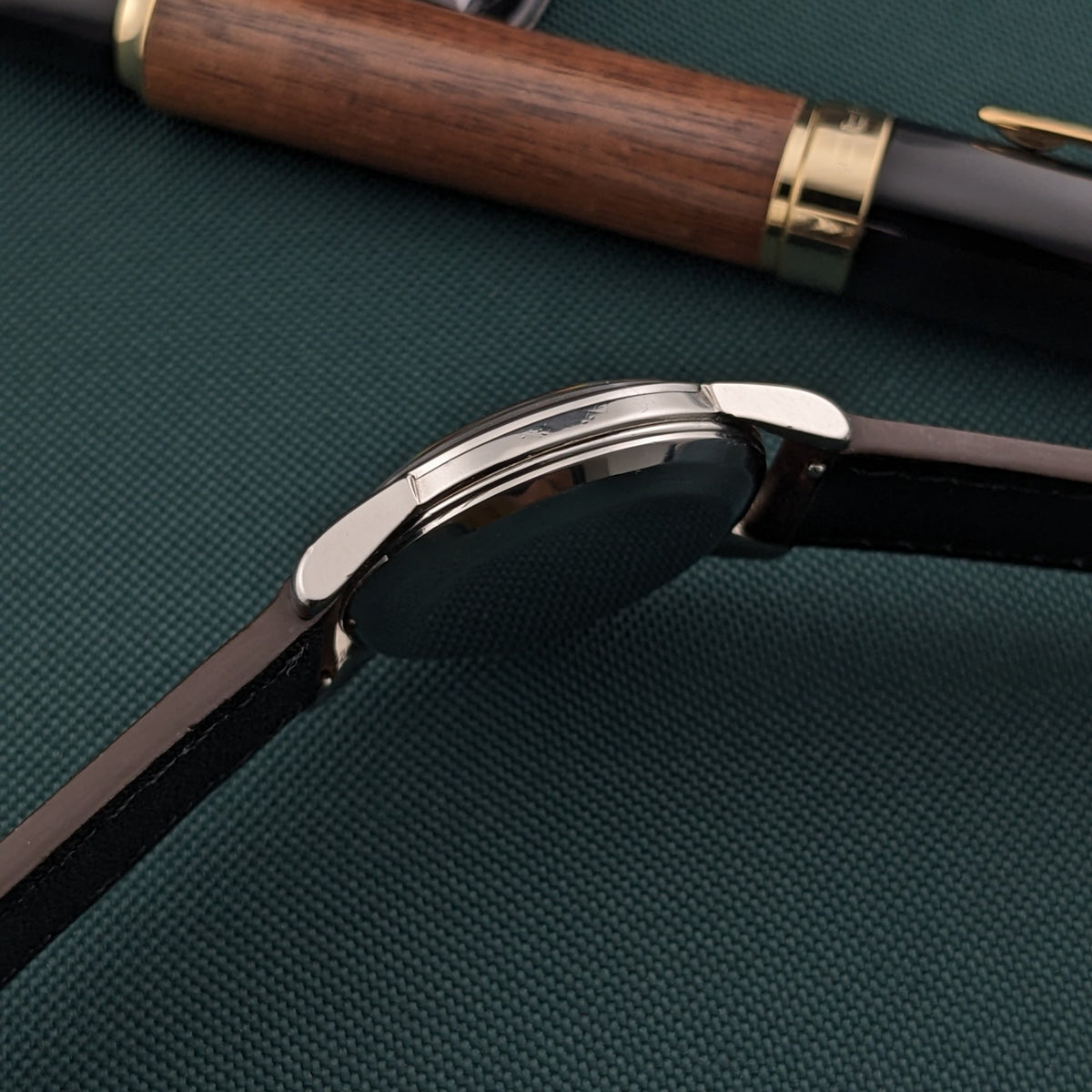 Omega Automatic Bumper reference 2767-4 SC shown in close side profile with curved case edges and a dark leather strap on green fabric.