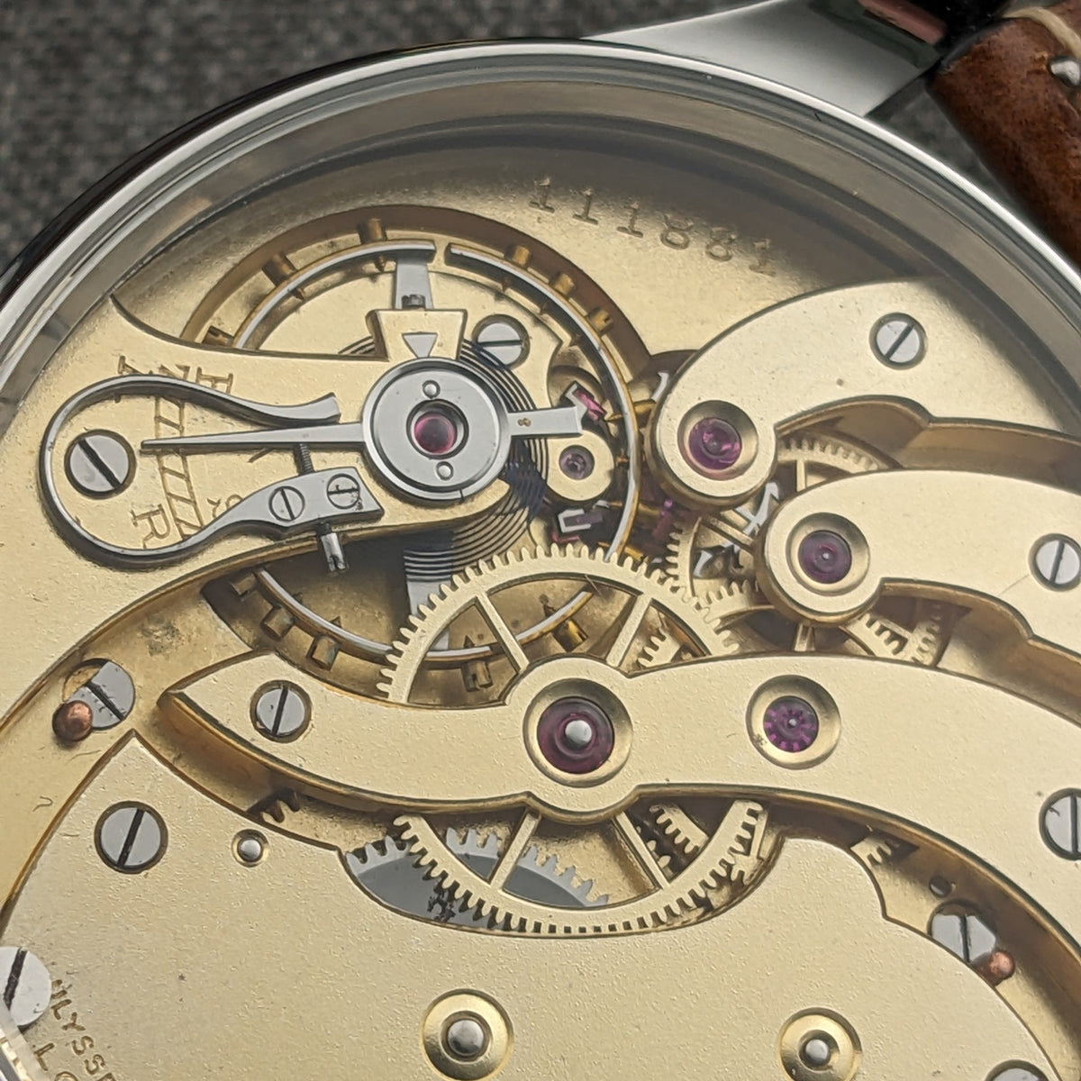 Ulysse Nardin यांत्रिक मूवमेंट का क्लोज़-अप, जिसमें ब्रिज, स्क्रू, रूबी रंग के रत्न, गियर्स और उत्कीर्ण निशान दिखते हैं।