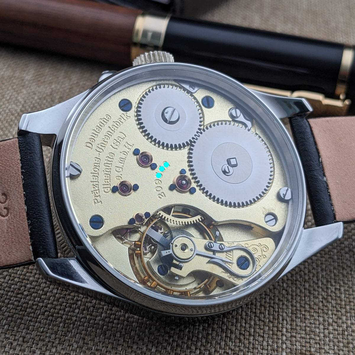 Rückansicht der Deutsche Präzisionsuhr „Original Glashütte” mit sichtbaren Zahnrädern, goldfarbenen Uhrwerksplatinen und Steinen