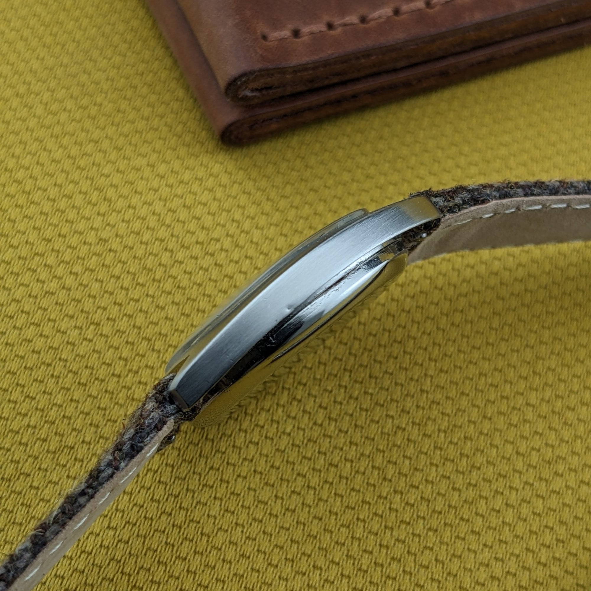 Side profile of the Omega Dr Ville Automatic ref. 162.045 against yellow fabric, highlighting the curved case edge and thin woven strap.