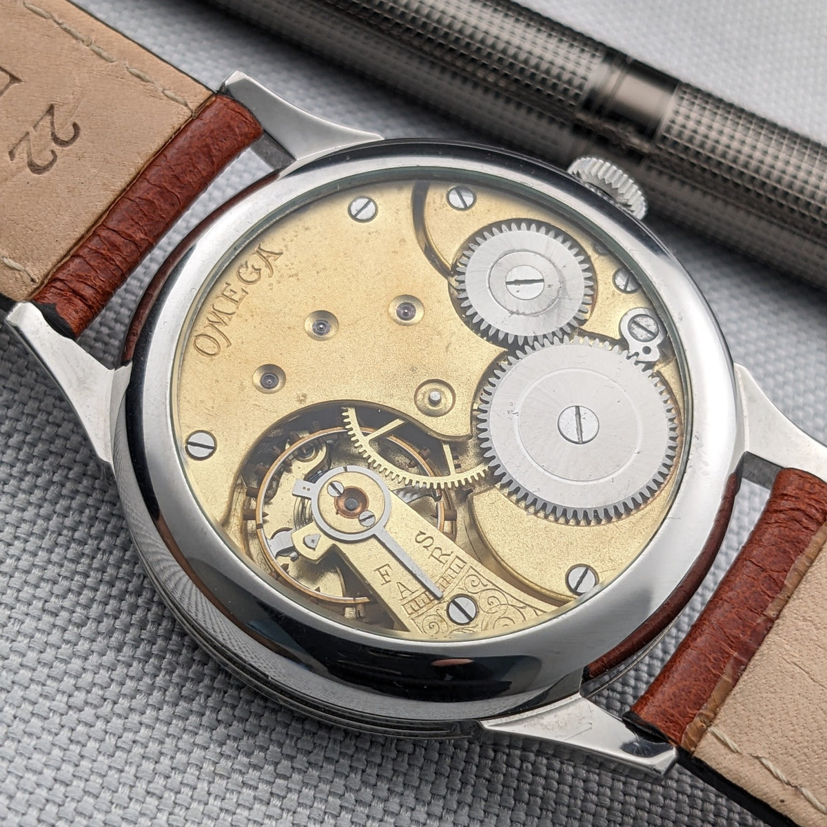 Nahansicht des Omega-Transparentgehäusebodens, der das mechanische Uhrwerk, Zahnräder, gravierte Platten und Enden des braunen Lederarmbands zeigt.