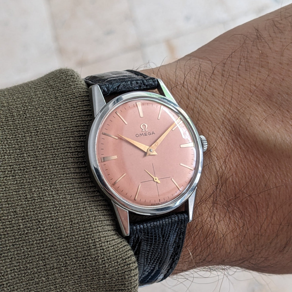 Primo piano dell'Omega Classic referenza 14391-1 al polso, evidenziando il quadrante rosa, la cassa argento, la corona e il cinturino nero testurizzato.