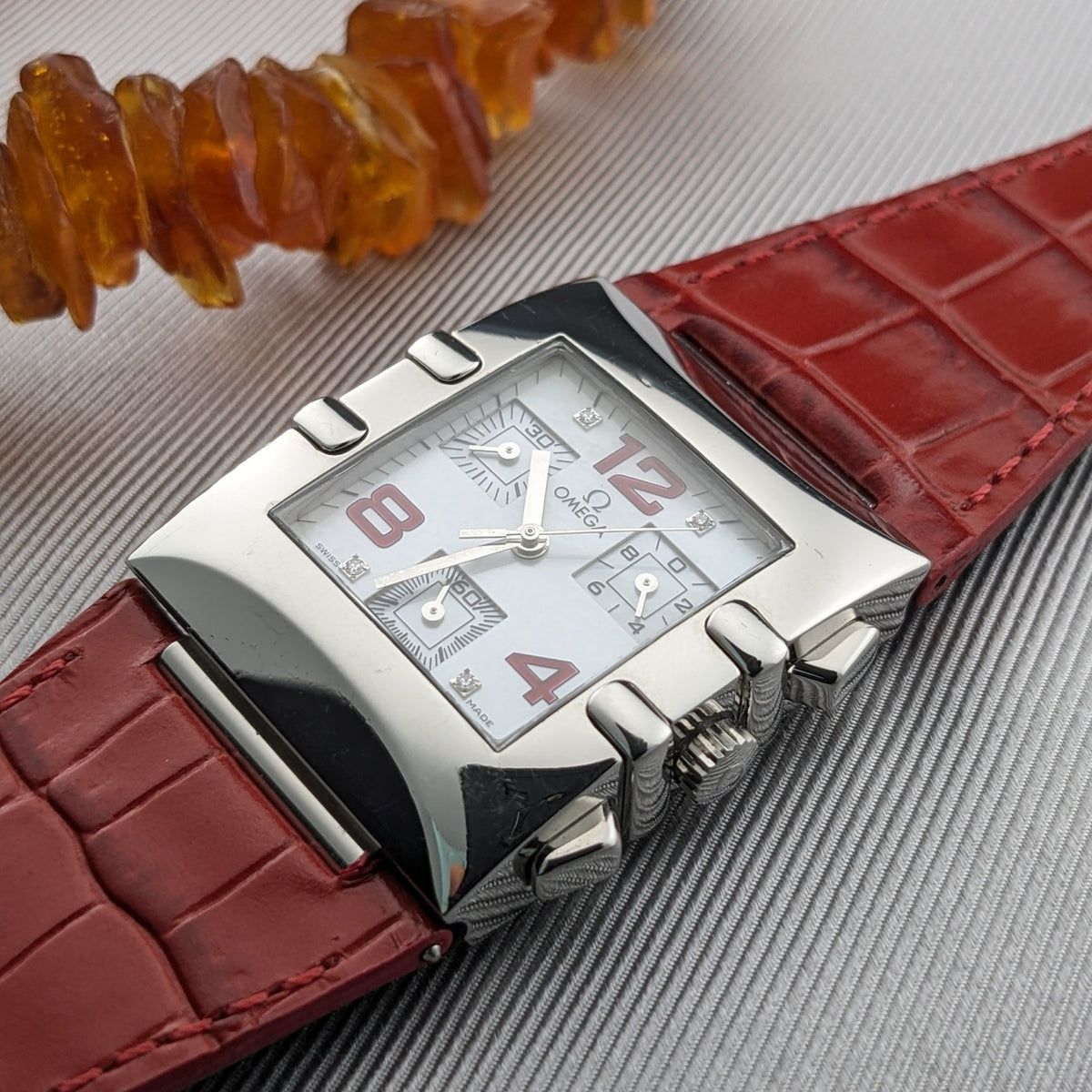 Detailed angled view of the Omega Constellation Quadra 1841.73.31 with red numerals, subdials, polished case, and red strap.