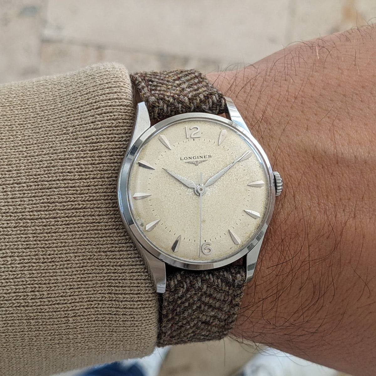 Close wrist close-up of the Longines Classic reference 8135-5, showing the cream dial, silver case, crown and textured brown strap.