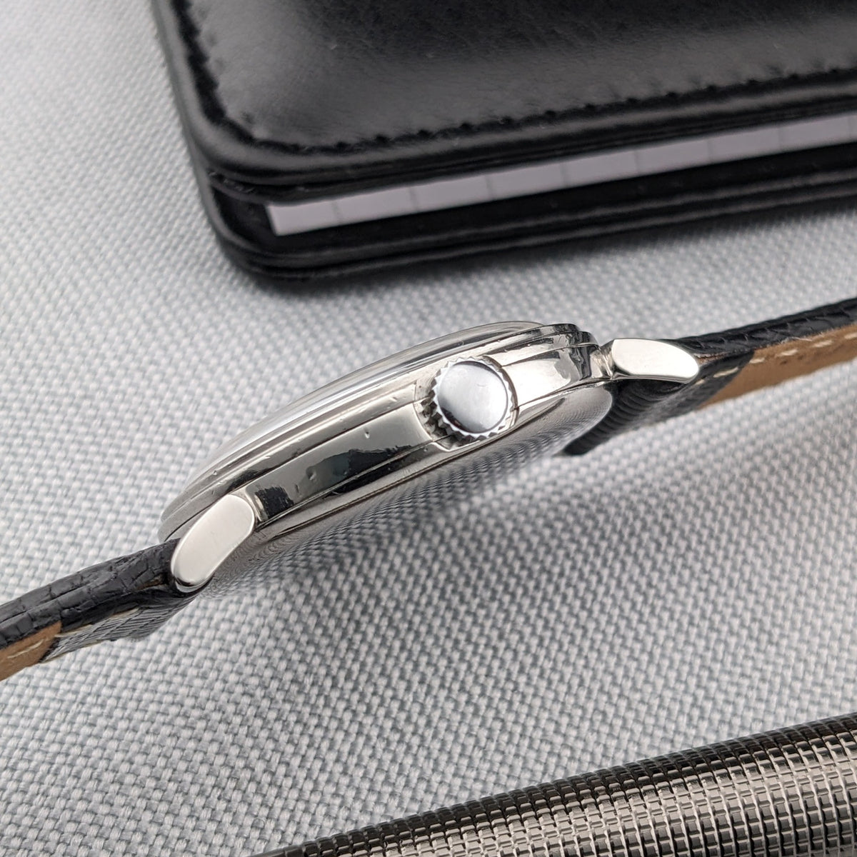 Side profile of the Omega watch showing its rounded case edge, winding crown, lugs and black strap.